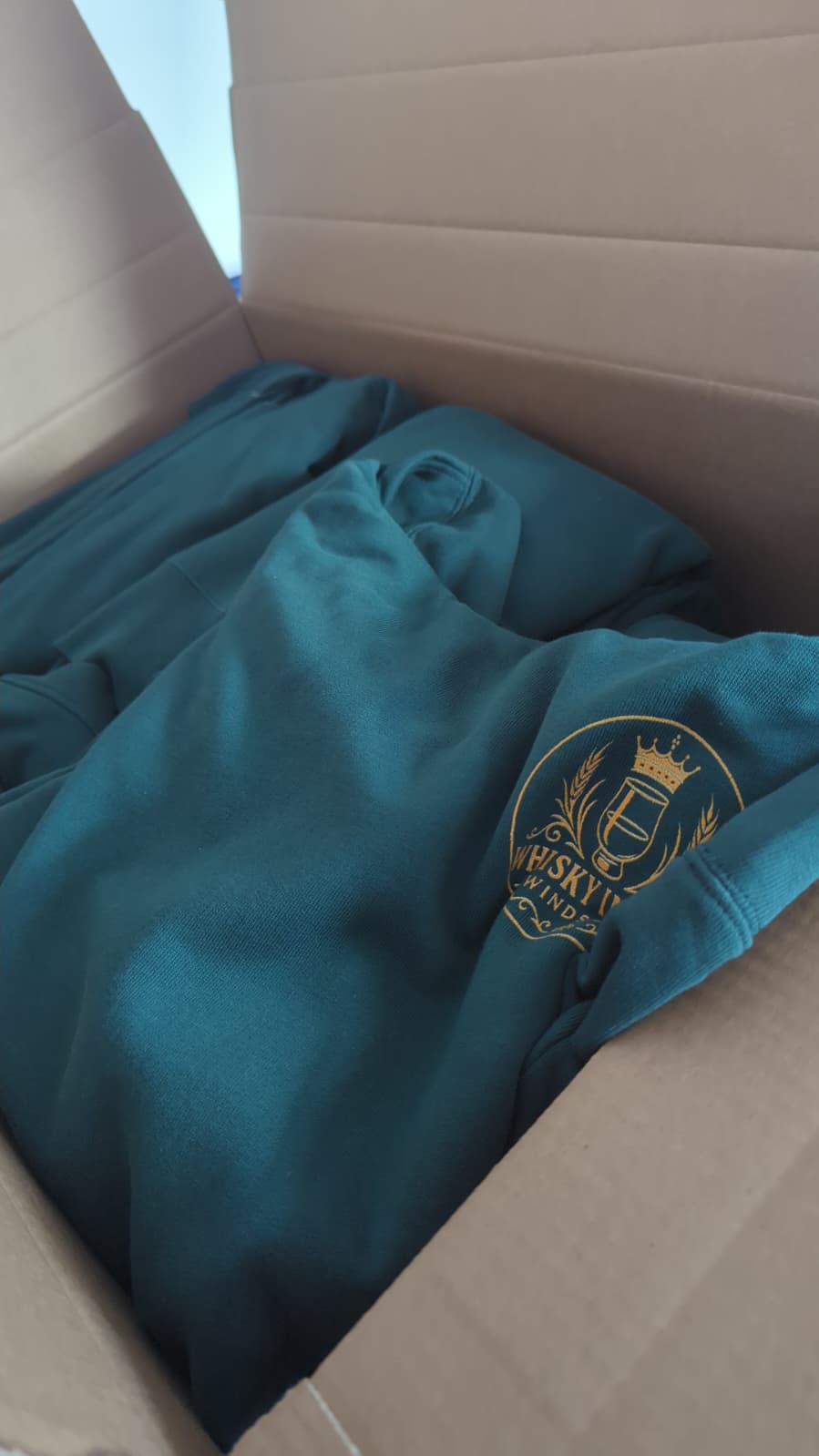 Karton mit petrolfarbenen Vereins-Hoodies mit goldenem Logo